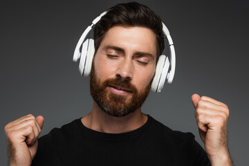 bearded man with closed eyed listening music in wireless headphones isolated on grey.