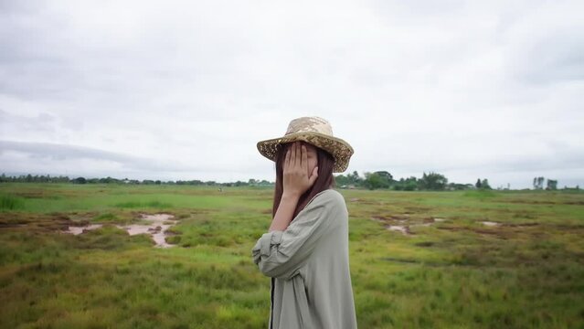 An Asian woman in a straw hat is embarrassed by covering her face with her hands.