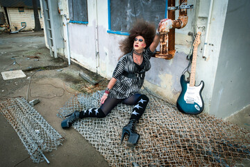 drag queen with big wig lying at abandoned building with guitar