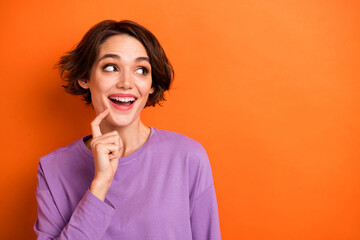 Portrait of cheerful minded girl finger touch chin look interested empty space isolated on orange color background