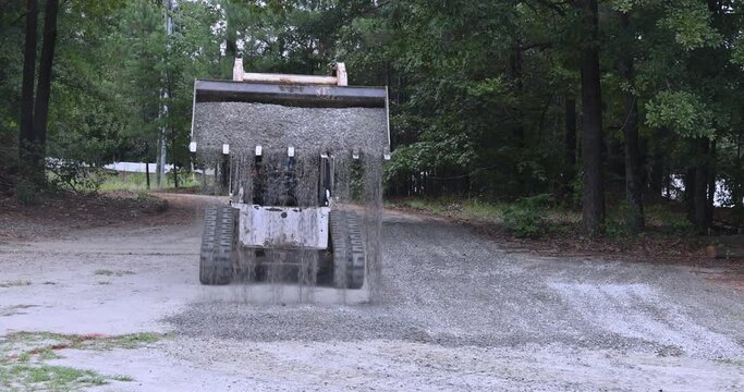 Bobcat tractor moving and unloading gravel on old road reconstruction site