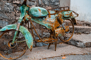 Fototapeta na wymiar an old rusty motorcycle of turquoise color stands disassembled against the background of a stone staircase. Close-up of the rusty details of an old two-wheeler.