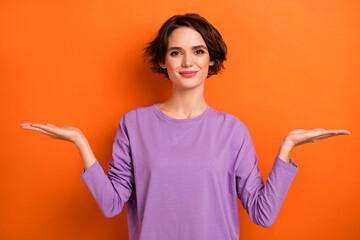 Photo of charming girl arms palms demonstrate empty space proposition isolated on orange color background