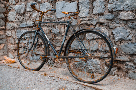 An old rusty two-wheeled bicycle stands against the background of a stone wall, ancient means of transportation.