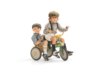 Cute happy kids riding tricycle isolated on white studio background. Retro vintage style concept. Friendship, hobbies, art, eras comparison