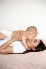 A beautiful young mother plays and cuddles with her baby in her bedroom on the bed. Love. motherhood Weasel tenderness. Lifestyle