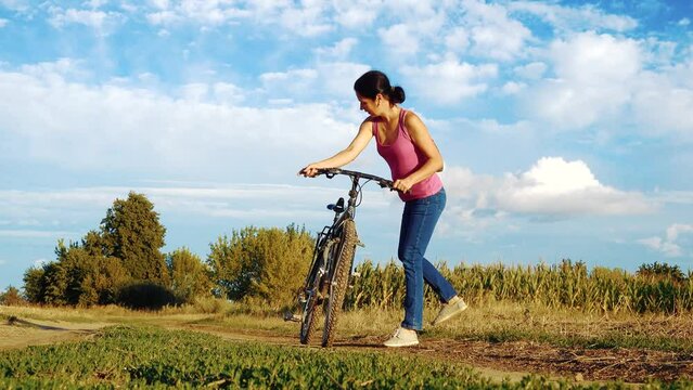 Young happy woman on a bike in the field. Girl rides a bike in nature. Close-up portrait, view from behind the grass. Camera movement.Concept of happiness, recreation, sports, nature.