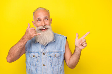 Photo of attractive dreamy man pensioner dressed denim vest showing phone sing pointing empty space isolated yellow color background