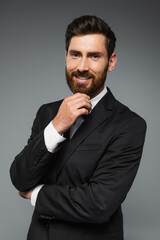portrait of cheerful and bearded man in elegant tuxedo with bow tie isolated on grey.