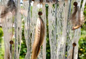 Dream catcher decorated with lace, threads, feathers and wooden beads outdoors in sunny weather
