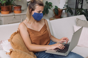 Young  sick woman working remotely at home in a protective face mask not to infect family members. 