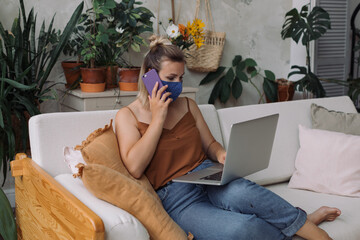 Young  sick woman working remotely at home in a protective face mask not to infect family members. Home isolation during virus infection or pandemic.
