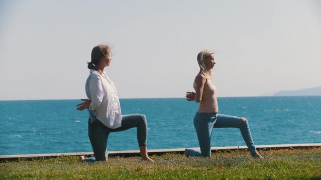 Two adult women doing simple gymnastics by the sea