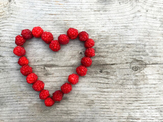 Raspberries laid out in a heart shape on a wooden background with copyspace