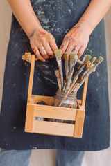 Woman in apron holding wooden box with art brushes. Closeup. Art, hobby concept.