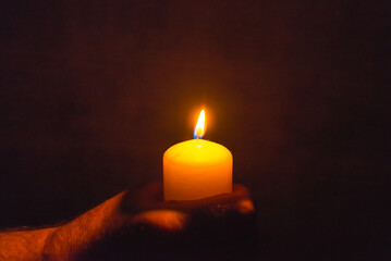 Burning candle in a mans hand religion concept.Candle in hands on a dark background.