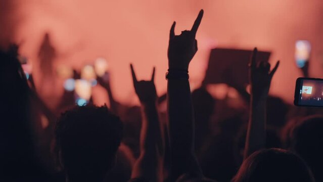A blurry and illuminated dancing crowd at a concert. An active and happy crowd at a late-night rock concert. Slow motion from a late-night rock concert. People are having fun, moving, raising their