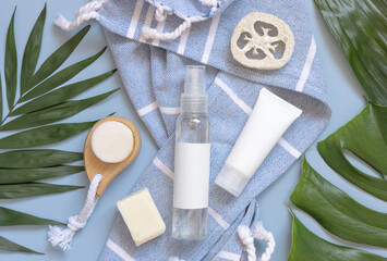 Fototapeta na wymiar Cosmetics spray dispenser bottle on blue bath towel near tropical leaves and skin care accessories, mockup