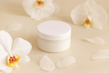 Fototapeta na wymiar Cream jar with a blank white lid near orchid flowers on light yellow close up. Cosmetic Mockup