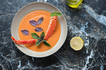 Plate of bisque with kamchatka crab and fresh basil on a black marble background, horizontal shot with space, view from above