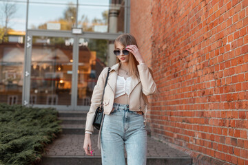 Fototapeta na wymiar Fashion stylish lifestyle urban woman in trendy leather jacket and vintage jeans wears a fashionable sunglasses and walks in the city