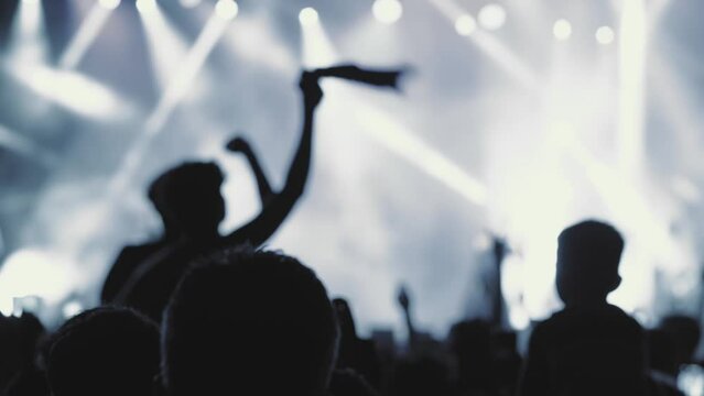 A blurry and illuminated dancing crowd at a concert. Silhouette of people at a party during the festival. People wave their hands, greeting their idol - musician, singer, rock star. The concert square