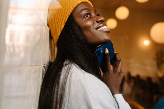 View through window on young smiling african woman holding phone