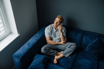 Young bearded man using cellphone while sitting on sofa at home