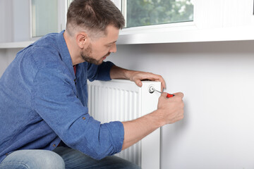 Man with screwdriver fixing radiator at home