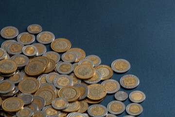 pile of mexican pesos coins, on a blue surface, with copy space