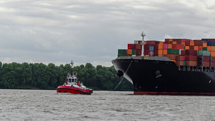 Fototapeta premium Containerschiff auf der Elbe bei Hamburg zusammen mit einem Schlepper