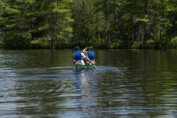 Couple in life vests paddling in a kayak on a lake surrounded by  thick coniferous forest, sunny summer day, selective focus. Water sports, recreation, adventure concept.