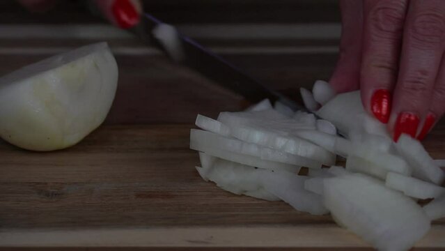 Closeup of a woman hands cut onion into slices with a knife