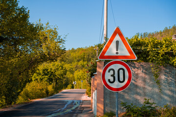 road signs warning of danger and limiting the maximum permissible speed to 30 kilometers per hour, Dangerous part of the road and speed-regulating signs against the background of the autumn forest