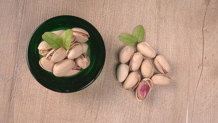 Pistachios or Pista nuts decorated with green leaves in glass bowl isolated on white background, top view.Flat lay.