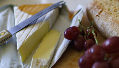 Summer lunch of rustic bread, brie and red grapes on a wooden chopping board