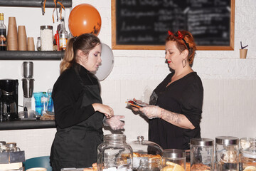 Experienced smiling middle aged woman owner of a cafe giving master class. Coffee Shop, Bar, Counter, Cafe Concept. Young entrepreneur conceptual. Halloween bakering. Preparing for Halloween party.