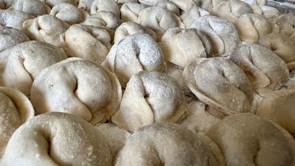  Sculpts dumplings and puts them on a wooden table, there are a lot of them, they are appetizing in flour and waiting to be cooked Each dumpling is full of meat, they are round and neatly handmade