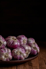 Violet garlic on a ceramic plate on a wooden background. Copy space.