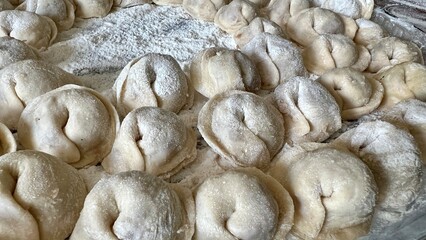  Sculpts dumplings and puts them on a wooden table, there are a lot of them, they are appetizing in flour and waiting to be cooked Each dumpling is full of meat, they are round and neatly handmade