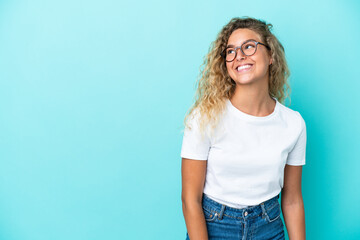 Girl with curly hair isolated on blue background thinking an idea while looking up