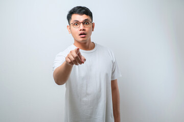 Young handsome asian man wearing casual shirt standing  pointing to you and the camera with fingers, shows shocked face