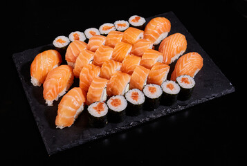 Big set of sashimi rolls with salmon, rolls California and Maki on a black flat board.