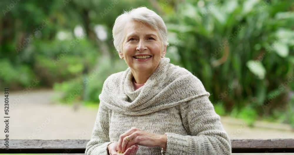 Poster Happy mature woman feeding birds while sitting in a park, smiling and enjoying simple pleasure of life. Senior female having solo fun interacting with nature, being playful and cheerful outdoors