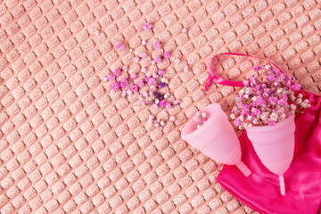 Two pink medical silicone menstrual cups with small pink flowers rest on a soft peach-colored fluffy fabric.  Lots of empty space
