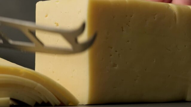 Knife cuts cheese into slices. Close-up shot of piece of cheese. Delicious cheese in 4K, UHD