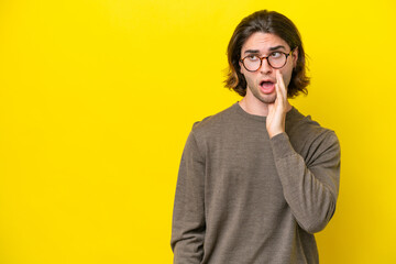Caucasian handsome man isolated on yellow background whispering something with surprise gesture while looking to the side