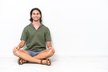 Young handsome man sitting on the floor isolated on white background laughing