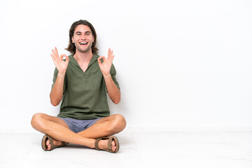 Obraz premium Young handsome man sitting on the floor isolated on white background showing an ok sign with fingers