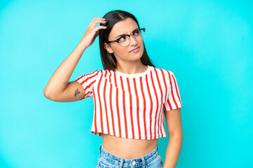 Young caucasian woman isolated on blue background having doubts while scratching head